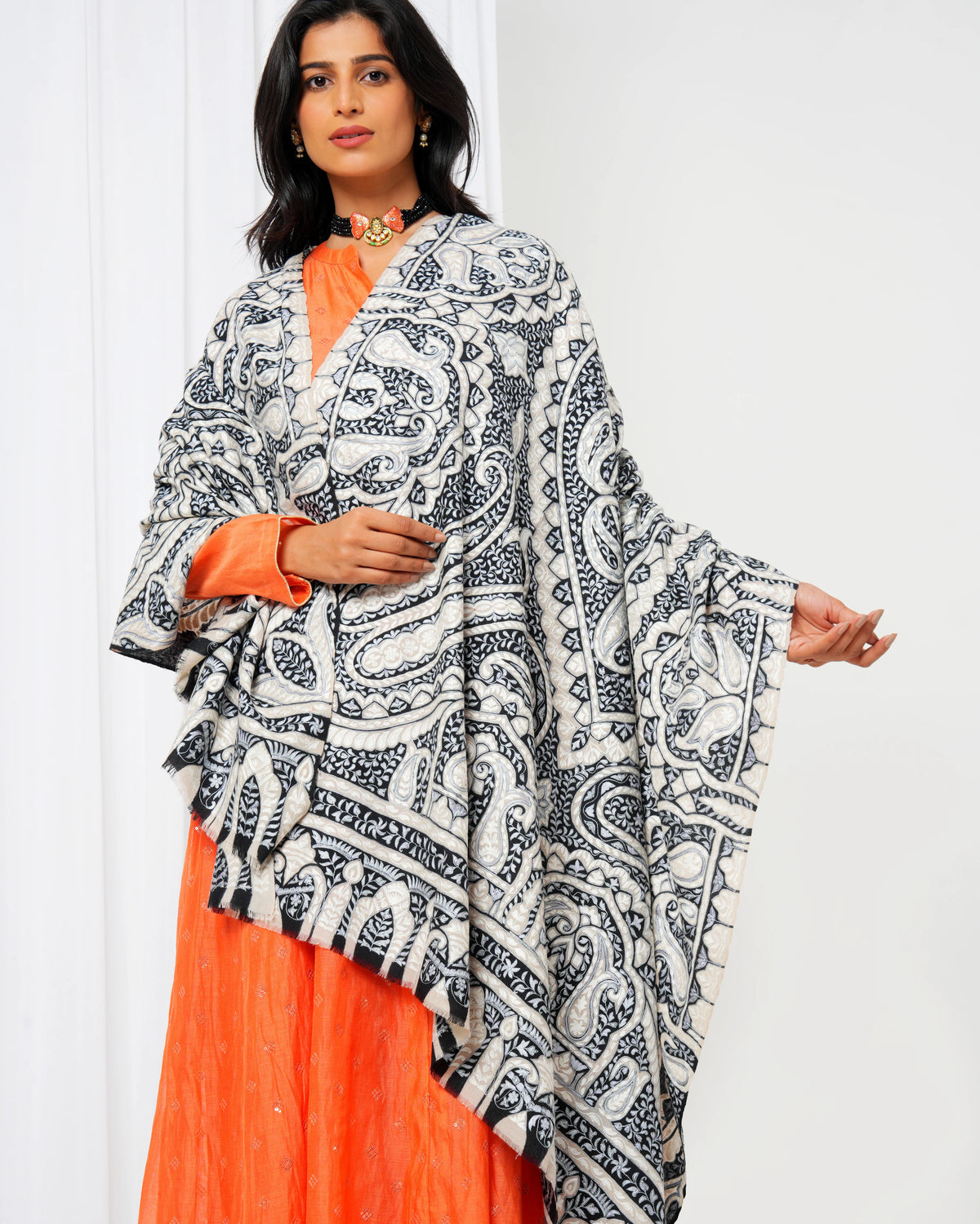 Woman wearing a black and white patterned dupatta over an orange outfit against a white background
