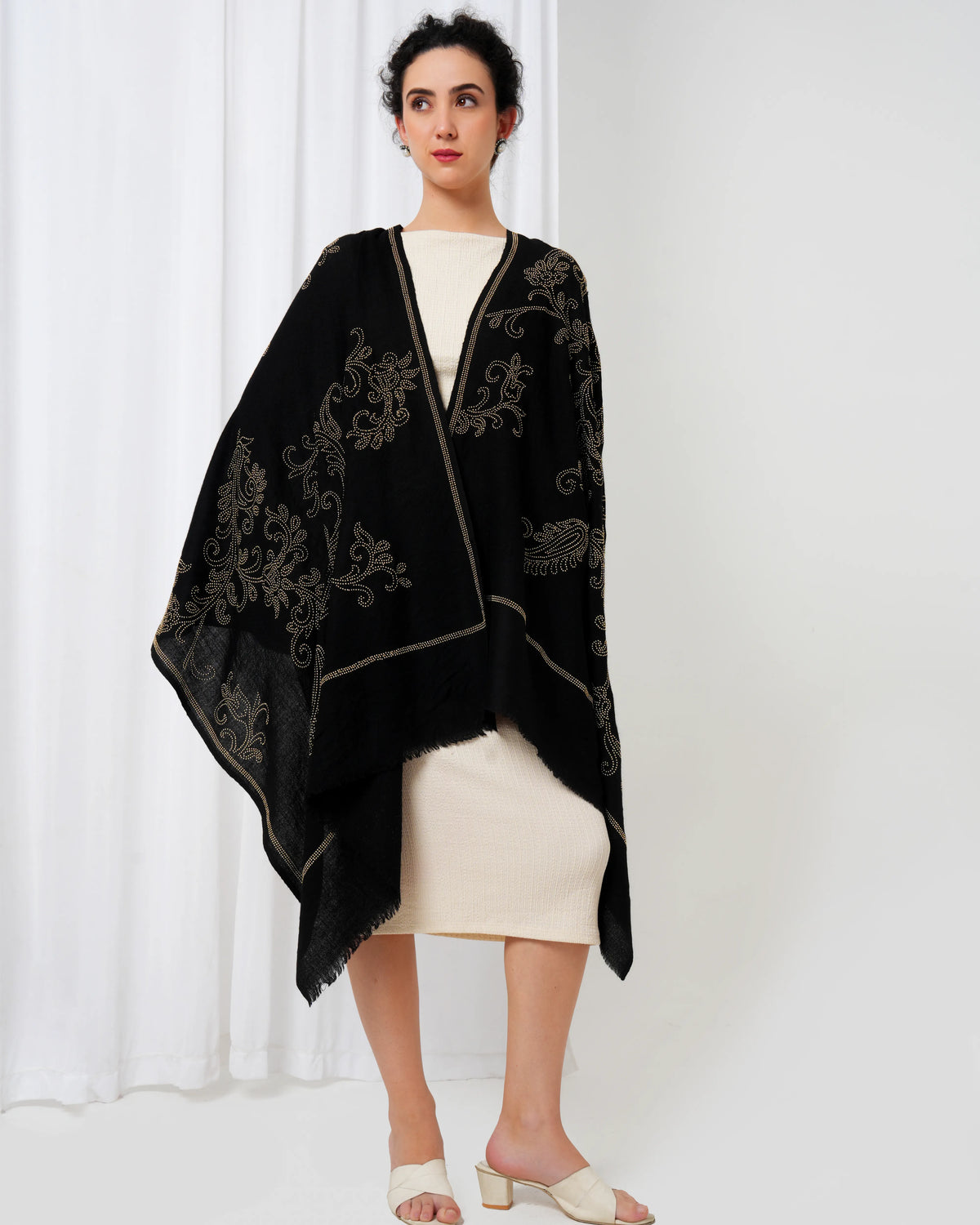 Woman wearing a black embroidered shawl over a white outfit against a white background