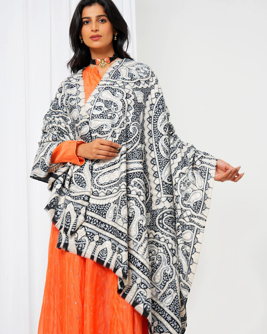 Woman wearing a black and white patterned dupatta over an orange outfit against a white background