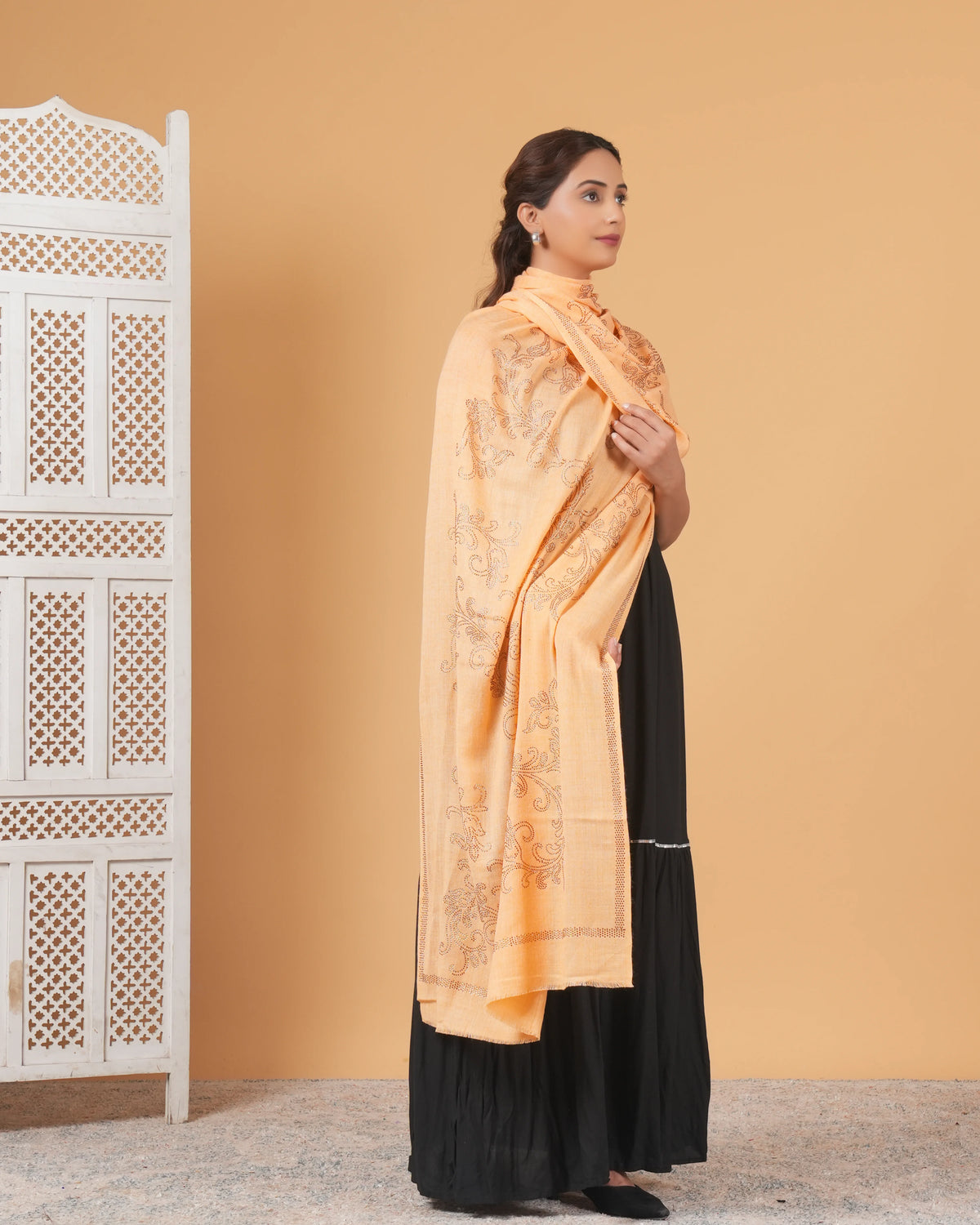 Woman wearing a peach shawl over a black dress against a beige wall.