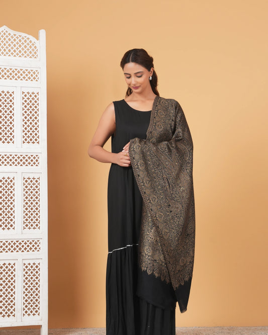 Woman holding a patterned shawl against an orange wall with a white lattice structure.