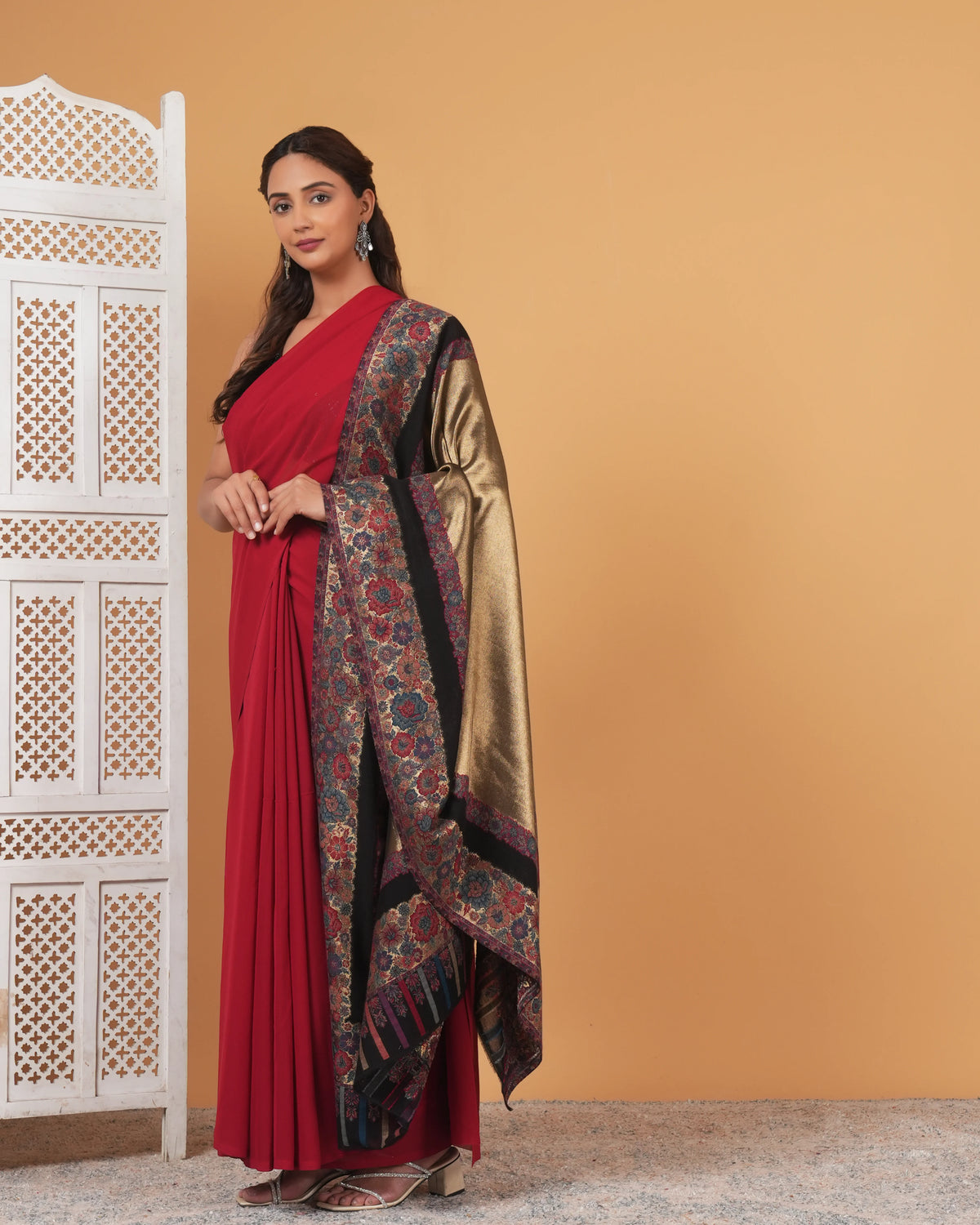 Woman in a red saree with a patterned shawl against a beige background