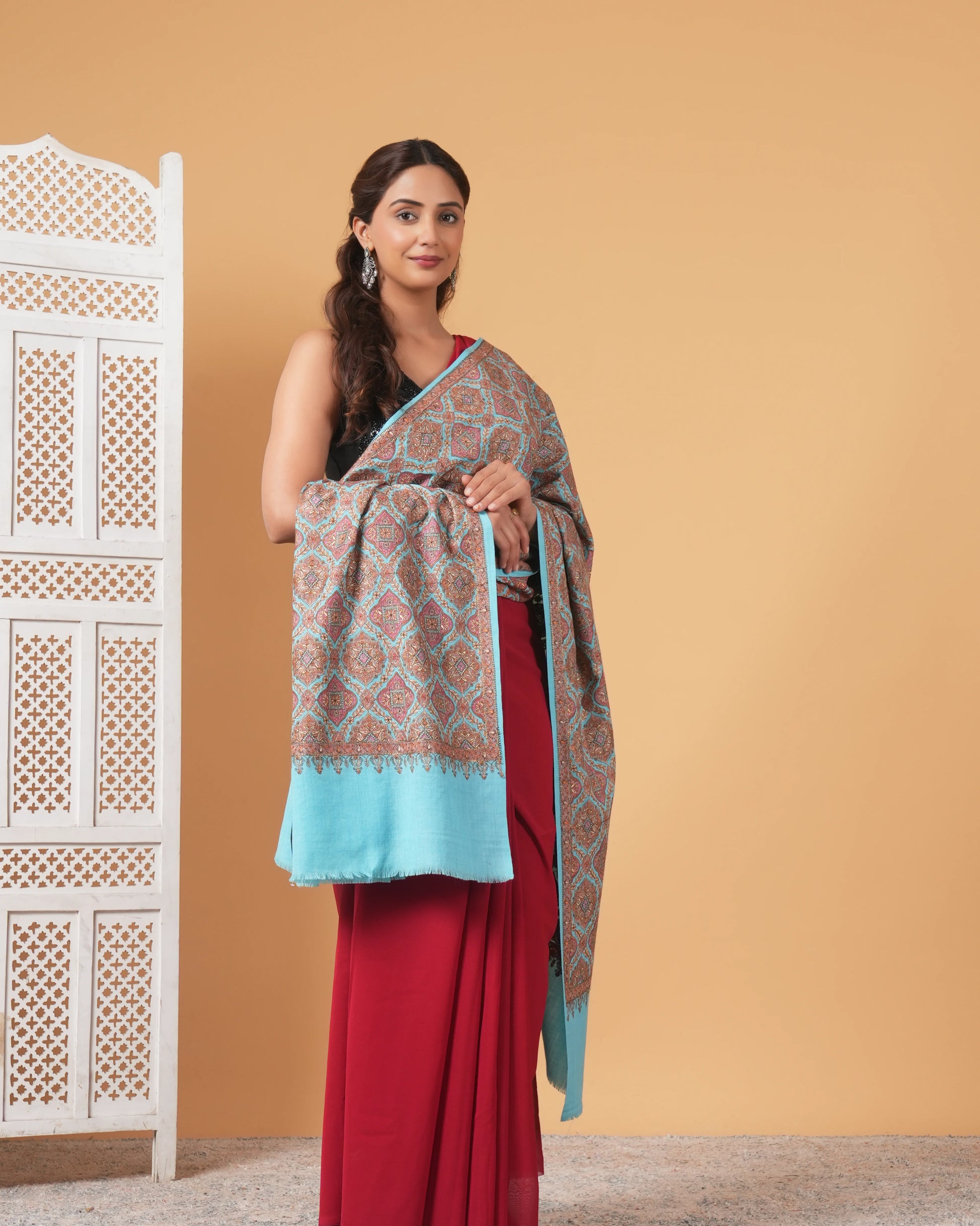 Woman wearing a red saree with a patterned shawl against a beige background
