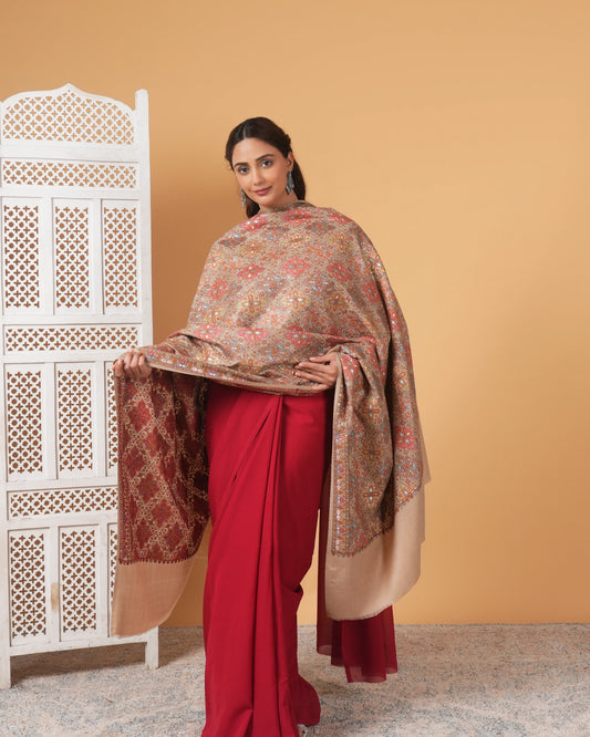 Woman wearing a red saree with a patterned shawl against a beige wall.
