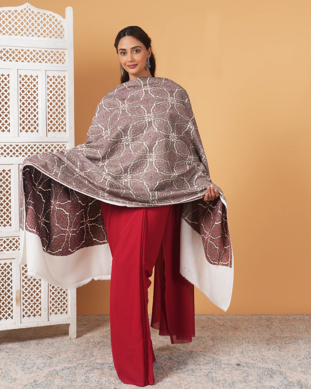 Woman wearing a patterned shawl over a red outfit against a beige wall.