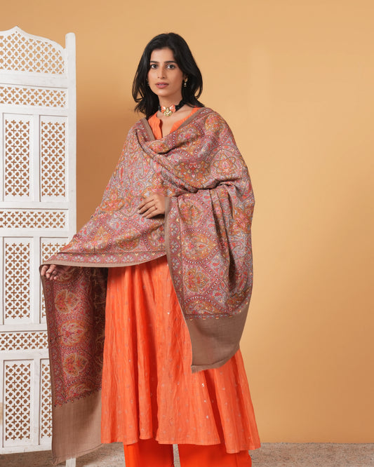 Woman wearing an orange traditional outfit with a patterned shawl against a beige background