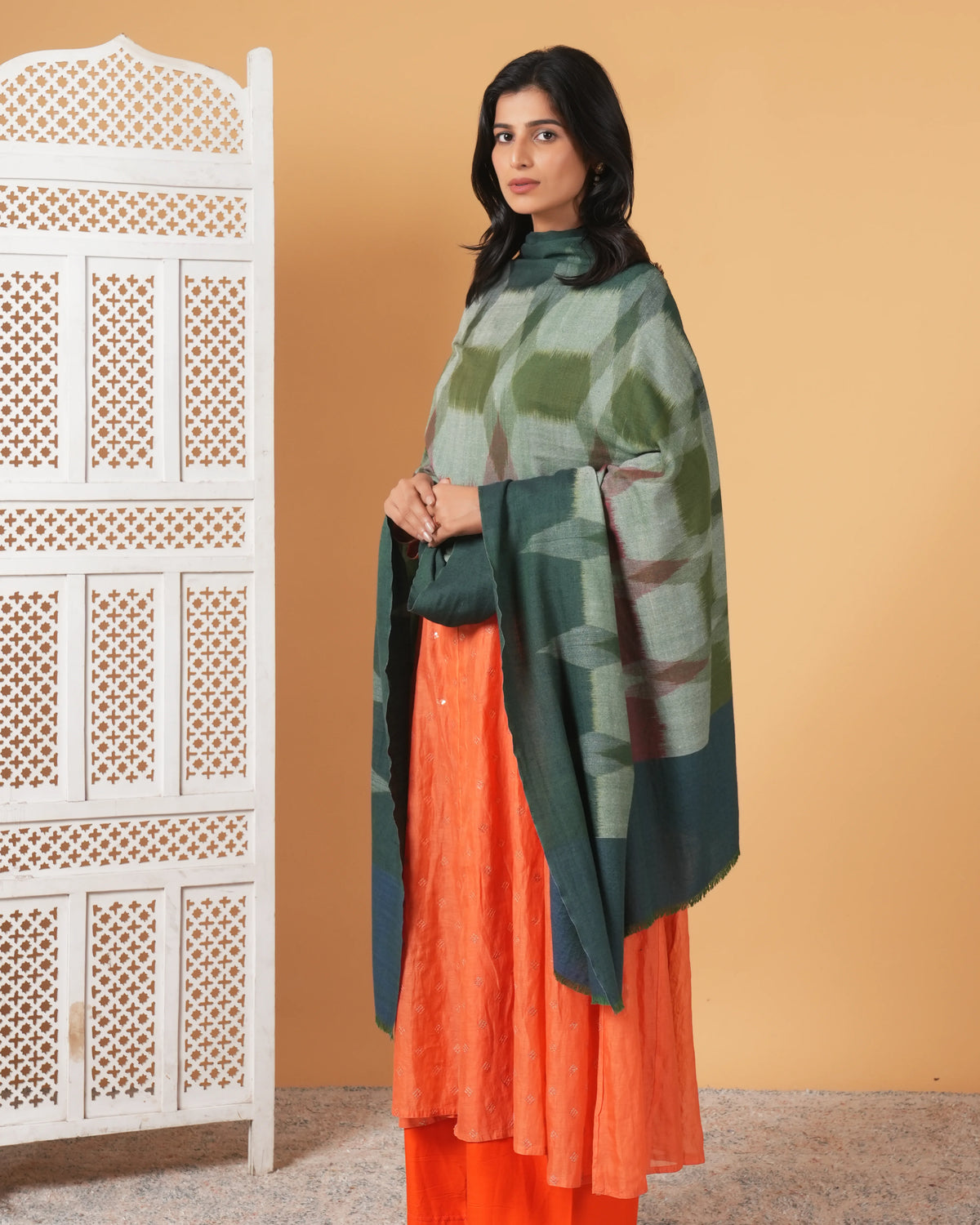 Woman wearing a green and orange traditional outfit with a patterned backdrop