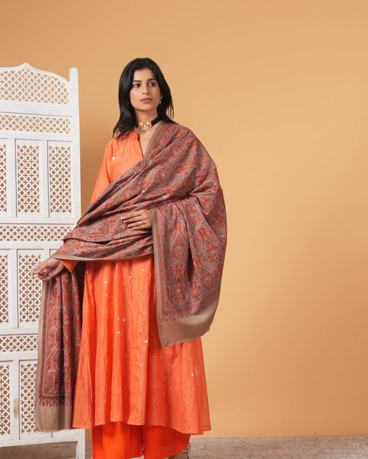 Woman wearing an orange traditional outfit with a patterned shawl against a beige background