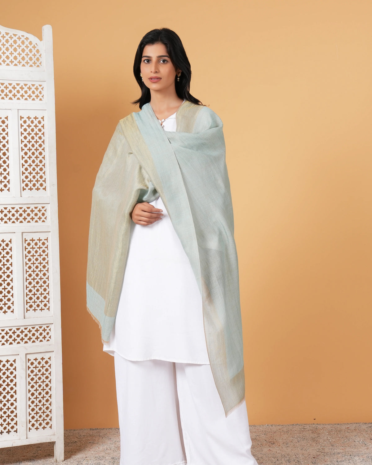 Woman wearing a light green dupatta over a white outfit against a beige wall.
