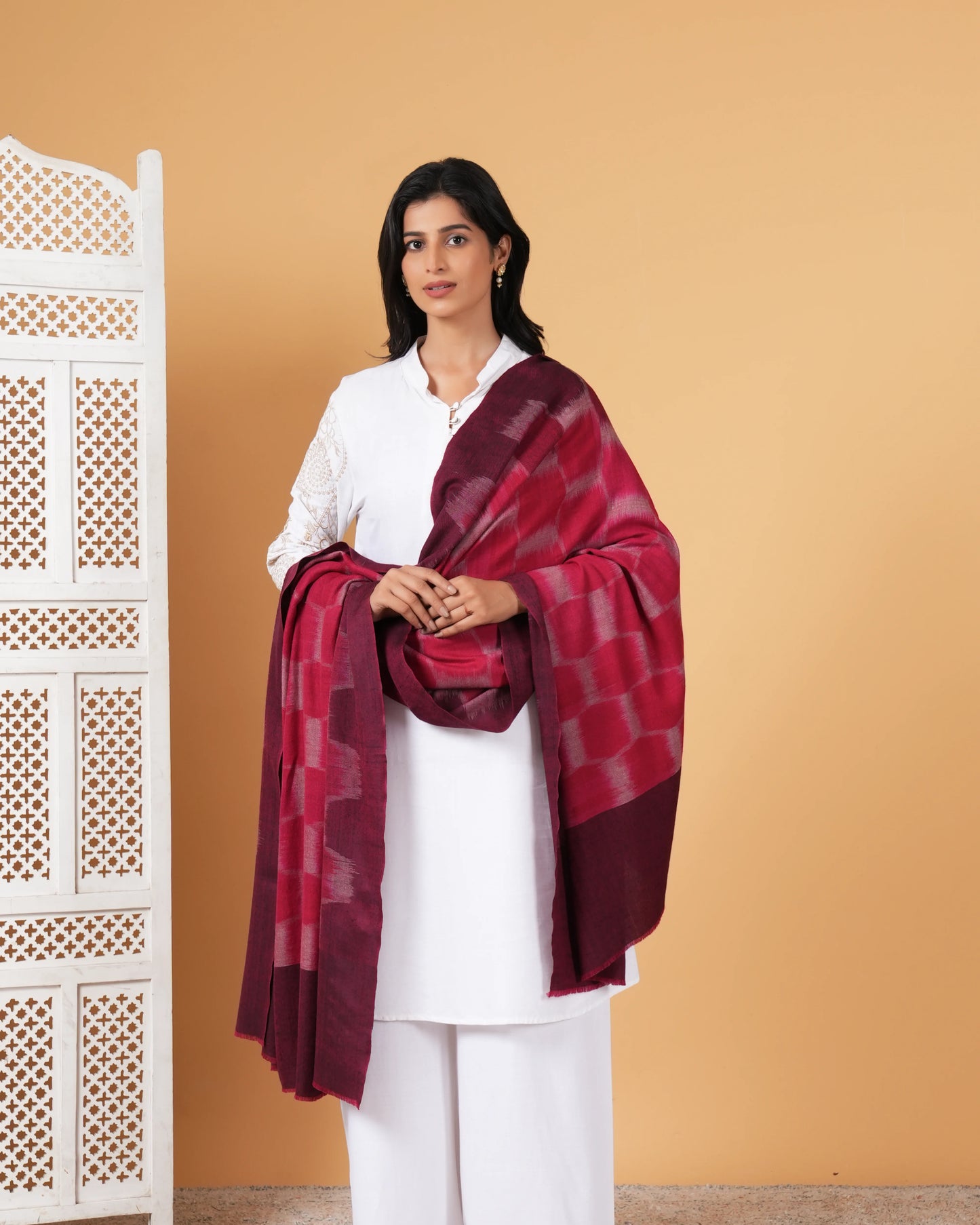 Woman wearing a maroon and white checkered scarf over a white outfit against a beige background