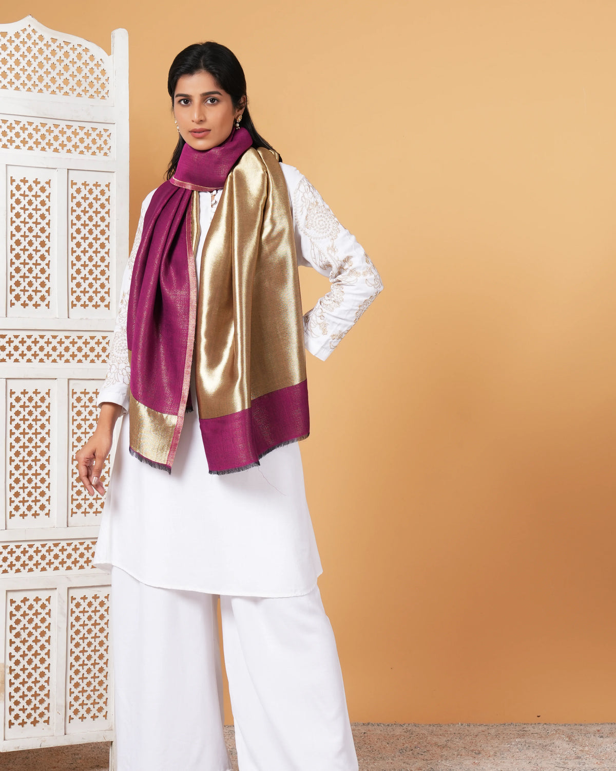 Woman wearing a gold and purple scarf against a beige wall.