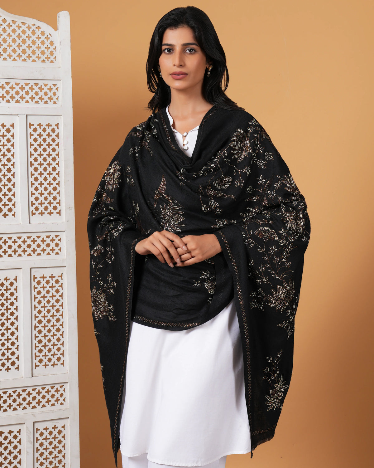 Woman wearing a black embroidered shawl over a white outfit against a beige background