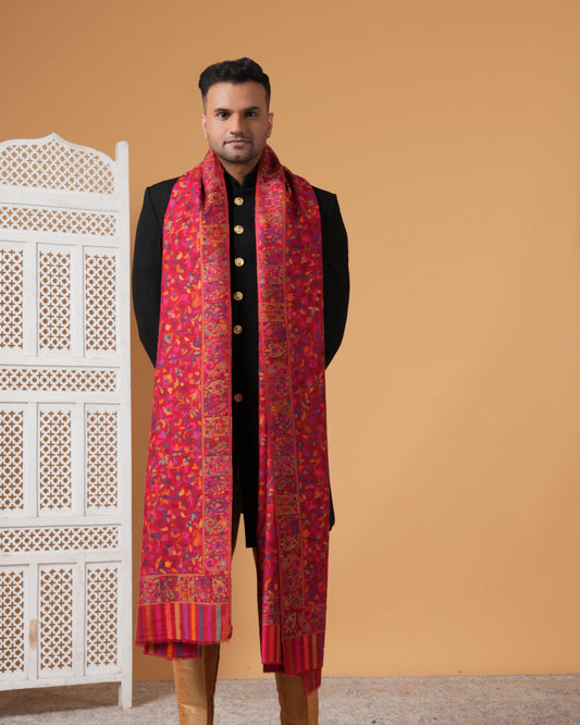 Man wearing a red patterned scarf with a black outfit against an orange wall.