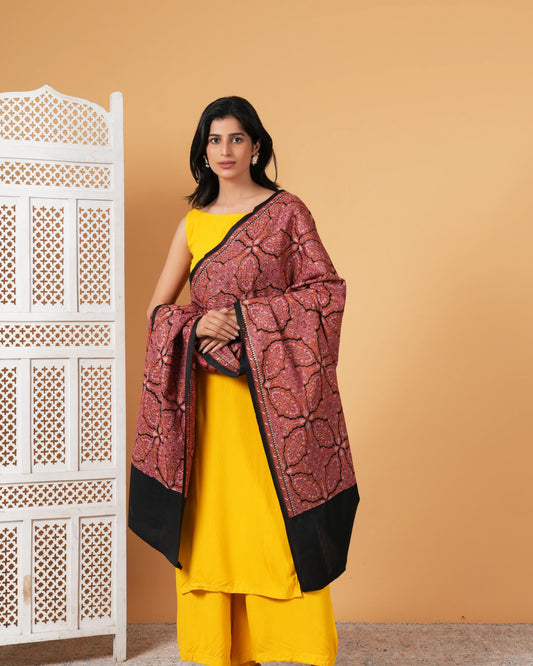 Woman wearing a yellow outfit with a maroon and black patterned shawl against a beige background.