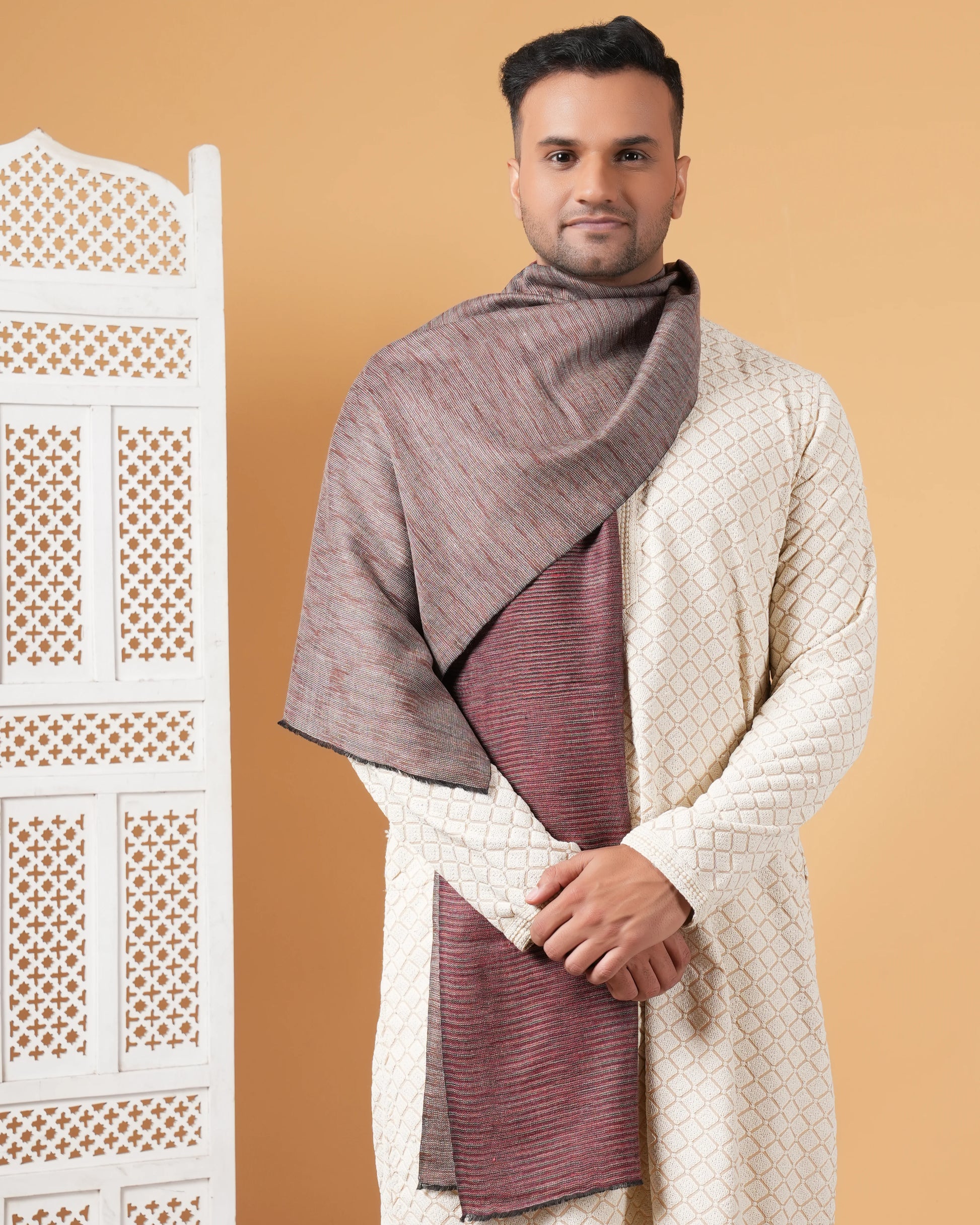 Man wearing a traditional outfit with a shawl against a beige background