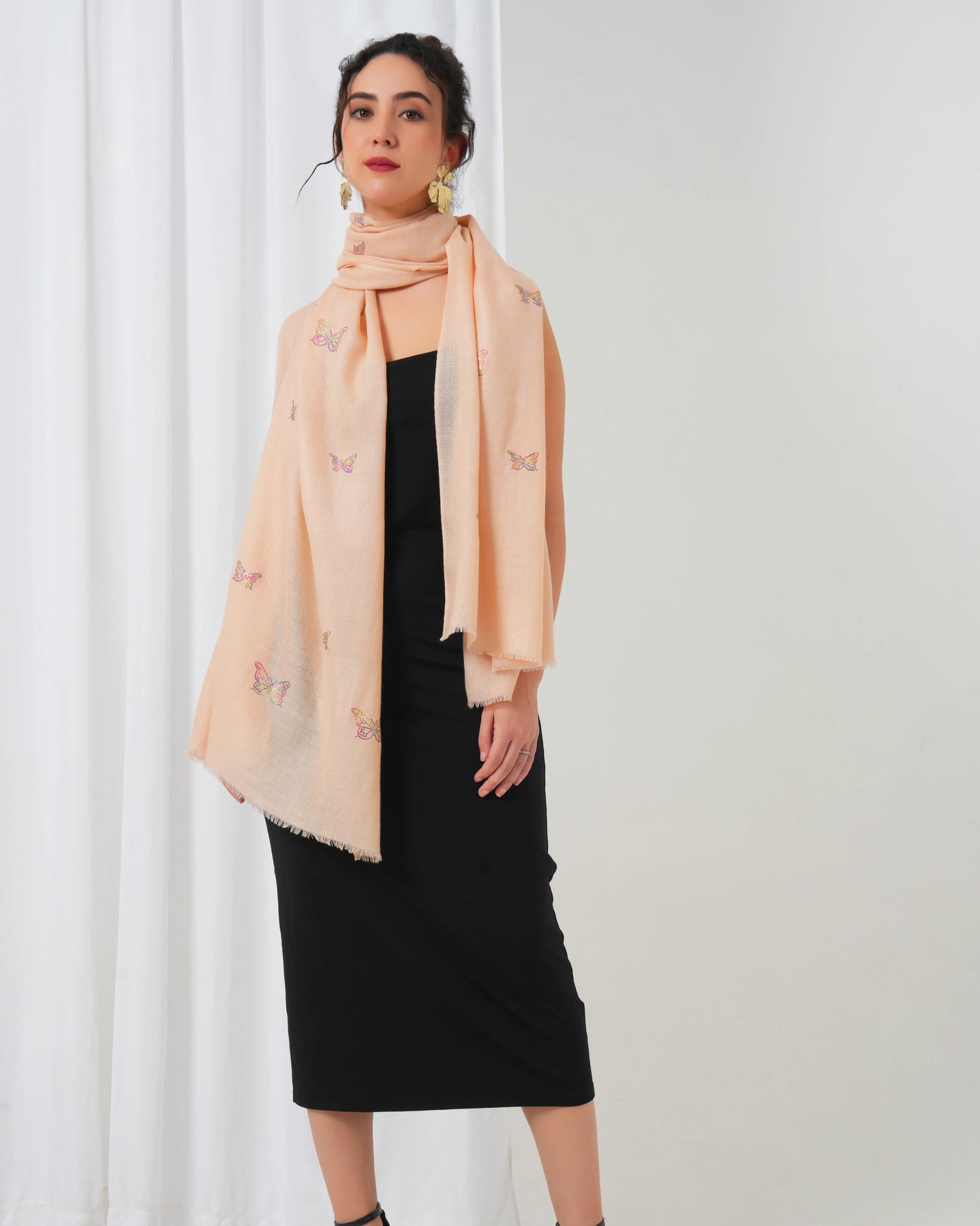 Woman wearing a peach scarf with butterfly patterns against a white curtain background