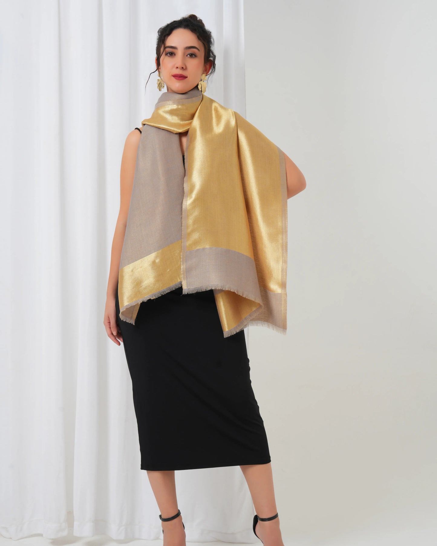 Woman wearing a gold and beige scarf against a white curtain background