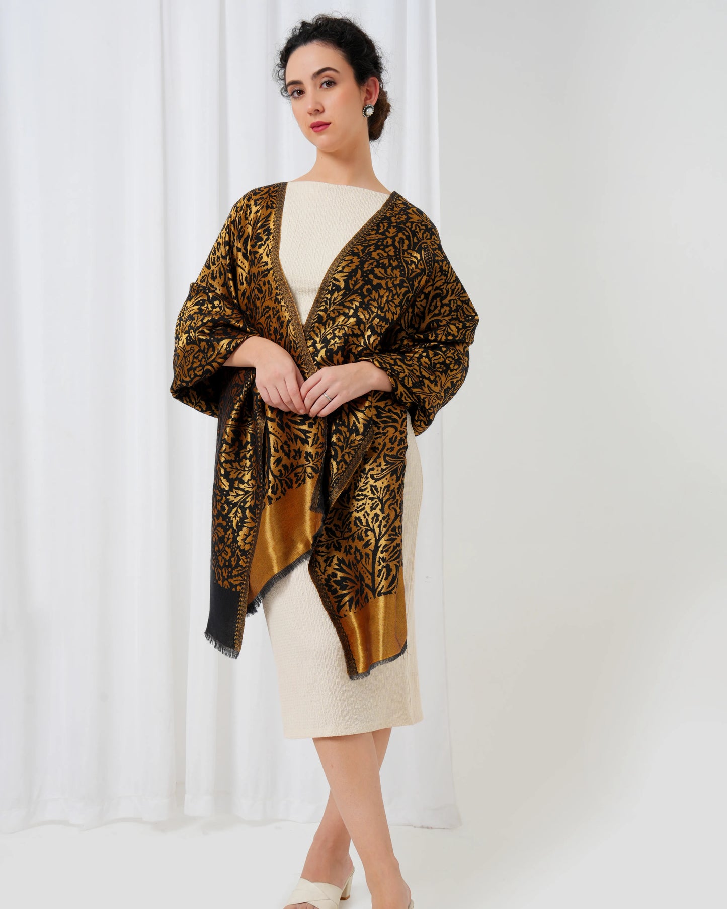 Woman wearing a patterned shawl over a plain dress against a white curtain background