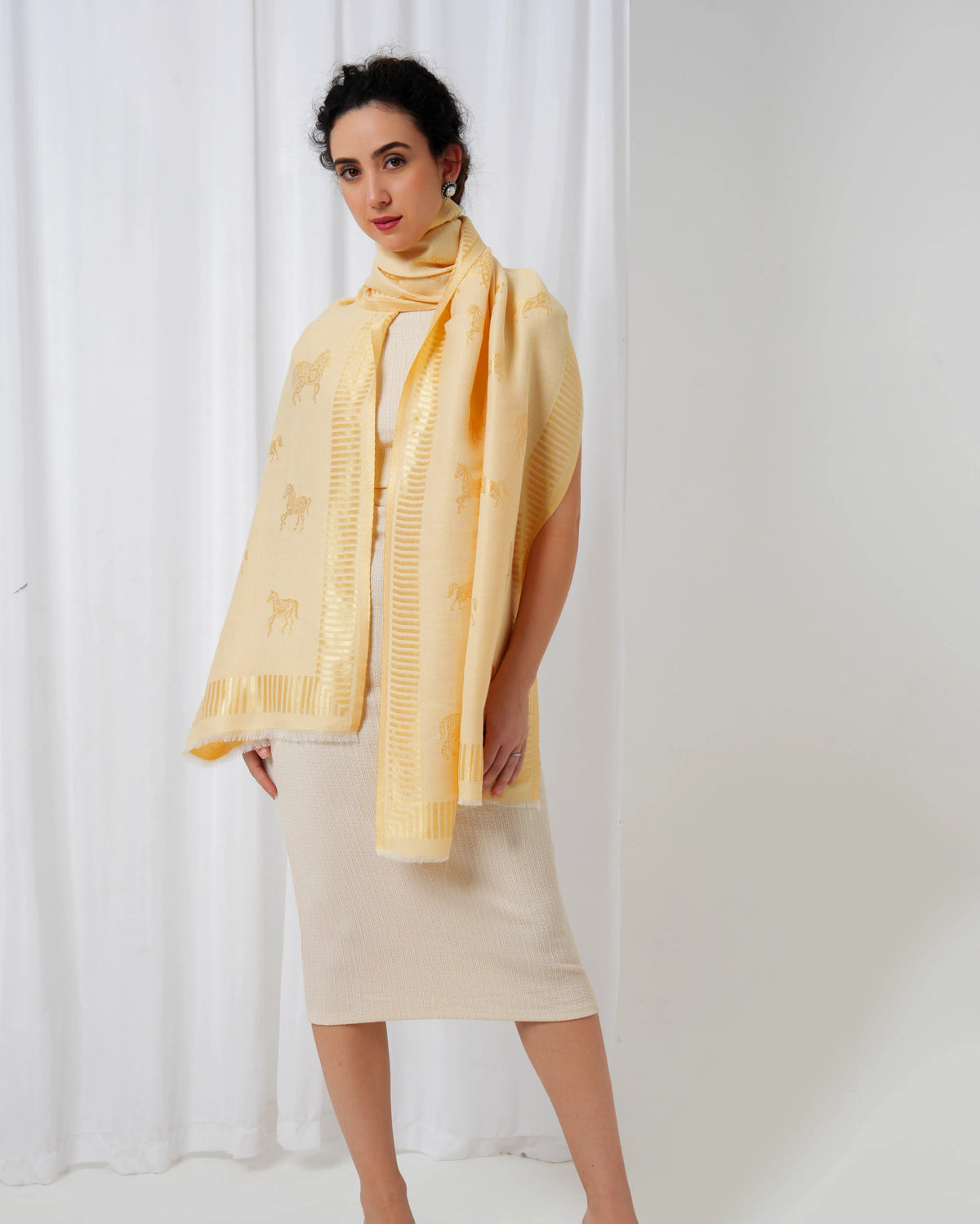 Woman wearing a yellow scarf and dress against a white curtain background
