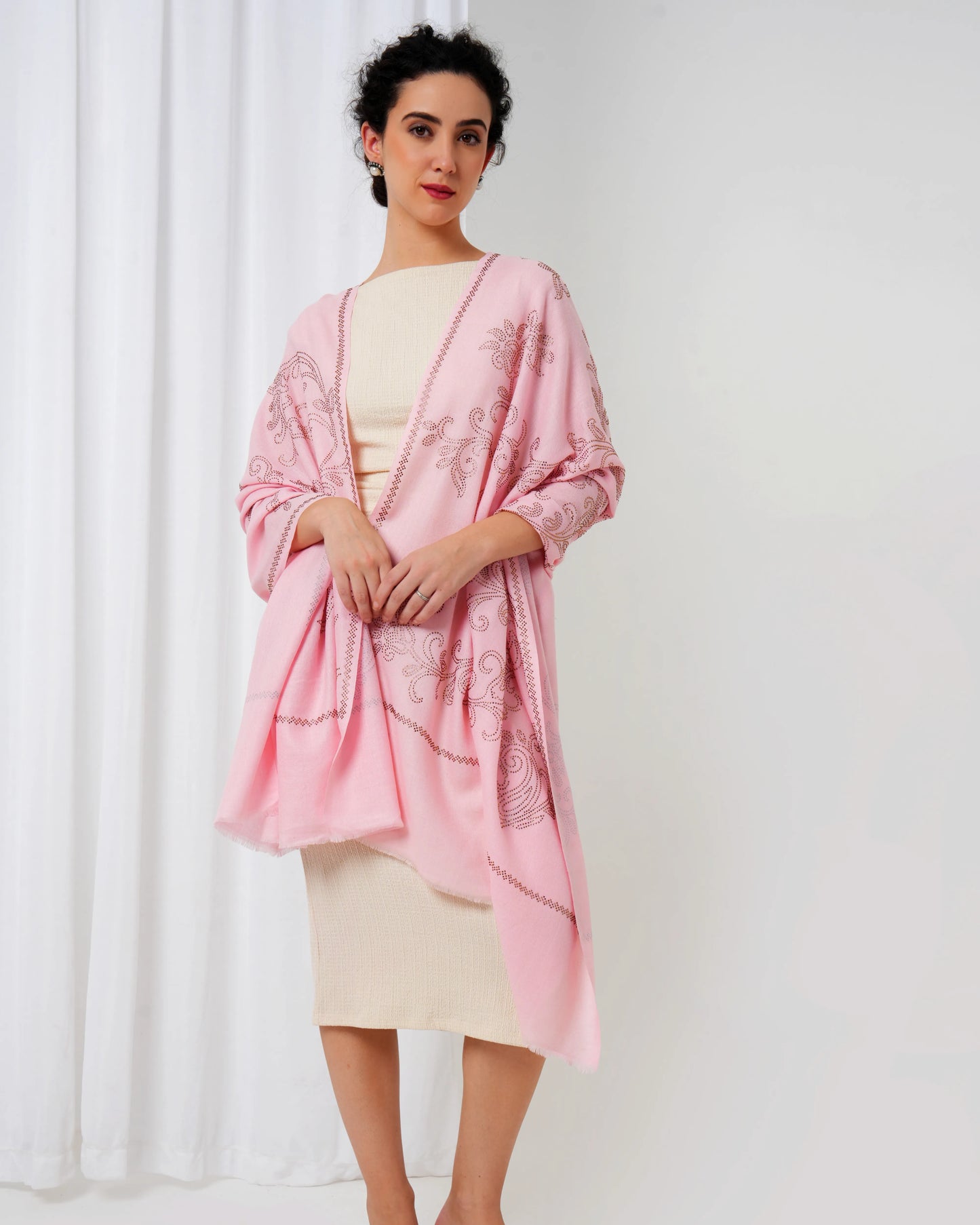 Woman wearing a pink embroidered shawl over a cream dress against a white background