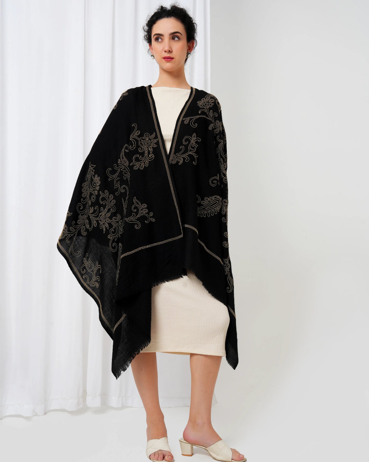 Woman wearing a black embroidered shawl over a white outfit against a white background