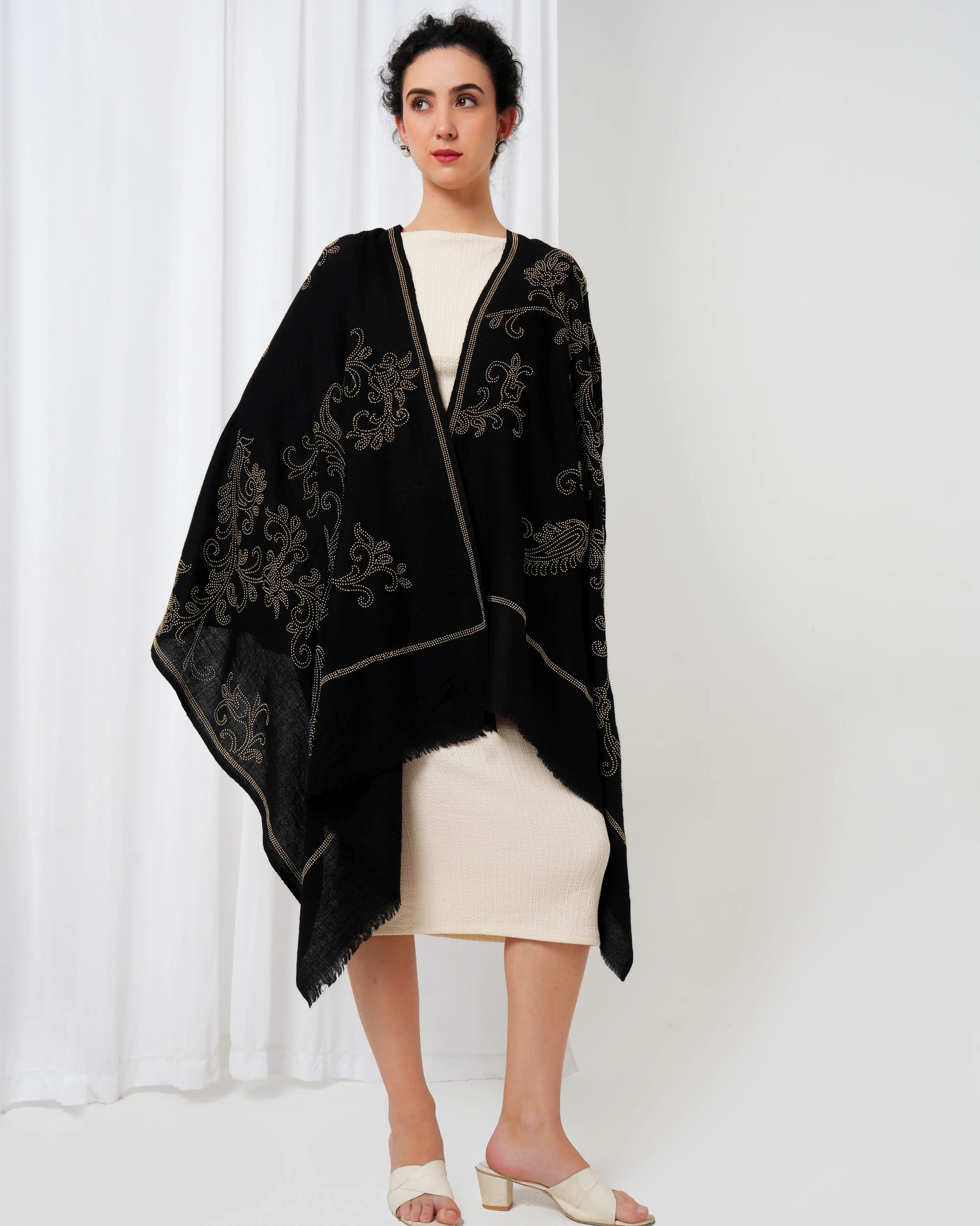 Woman wearing a black embroidered shawl over a white outfit against a white background