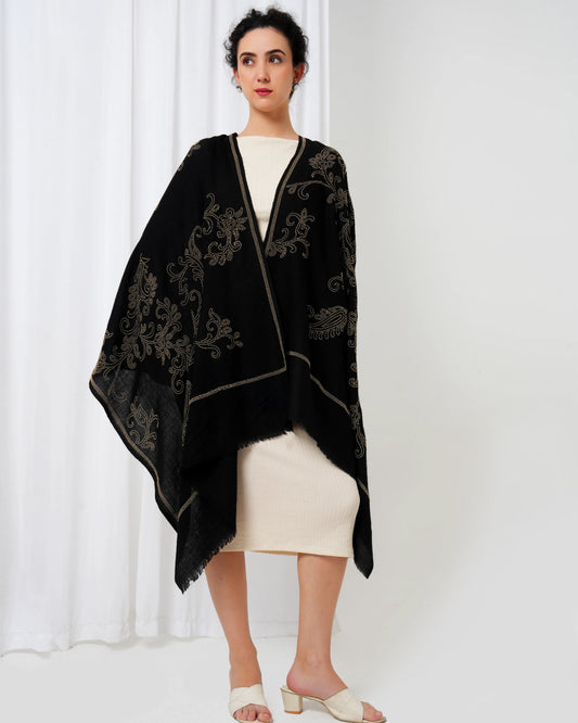 Woman wearing a black embroidered shawl over a white outfit against a white background