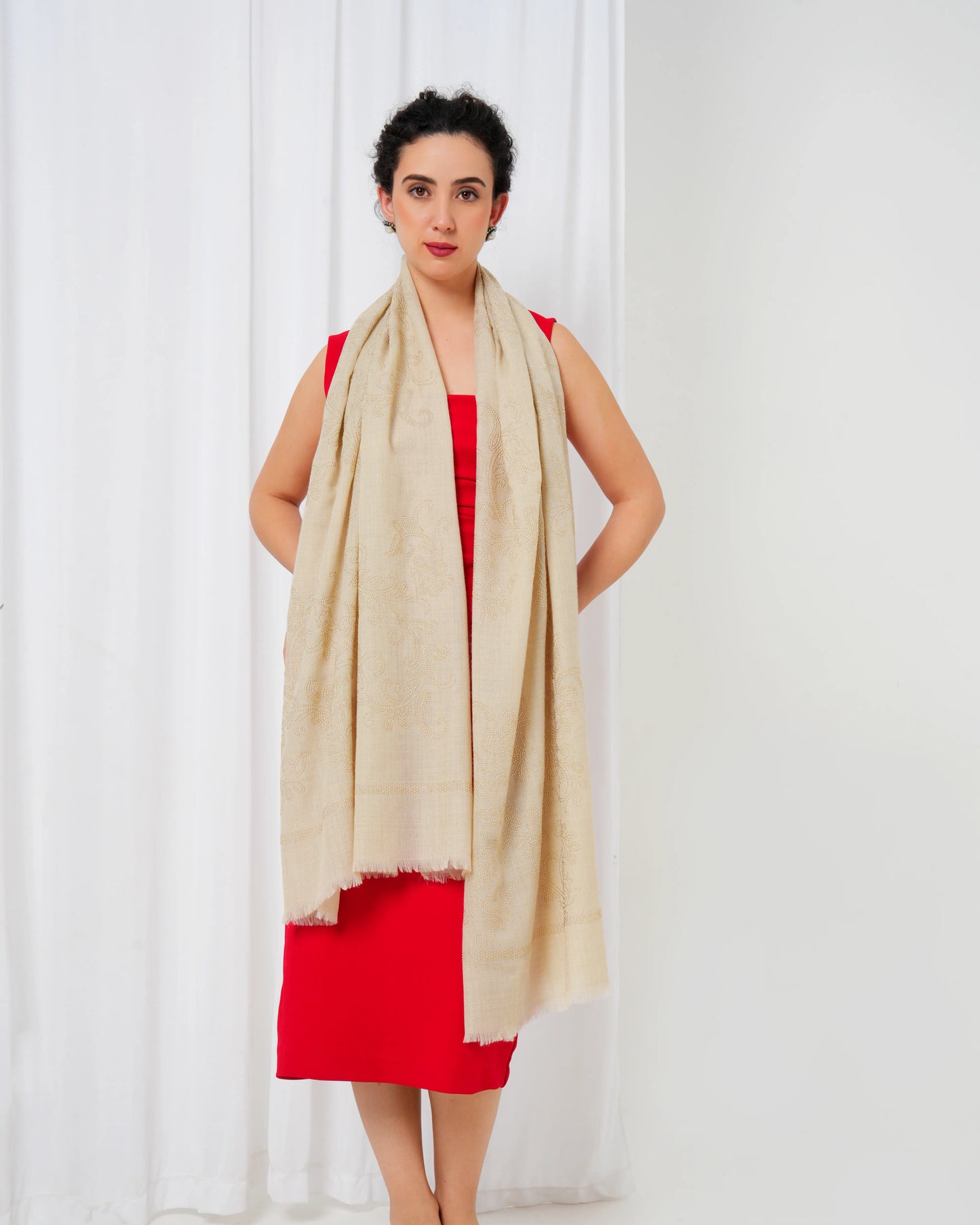 Woman wearing a red dress and beige scarf against a white curtain background