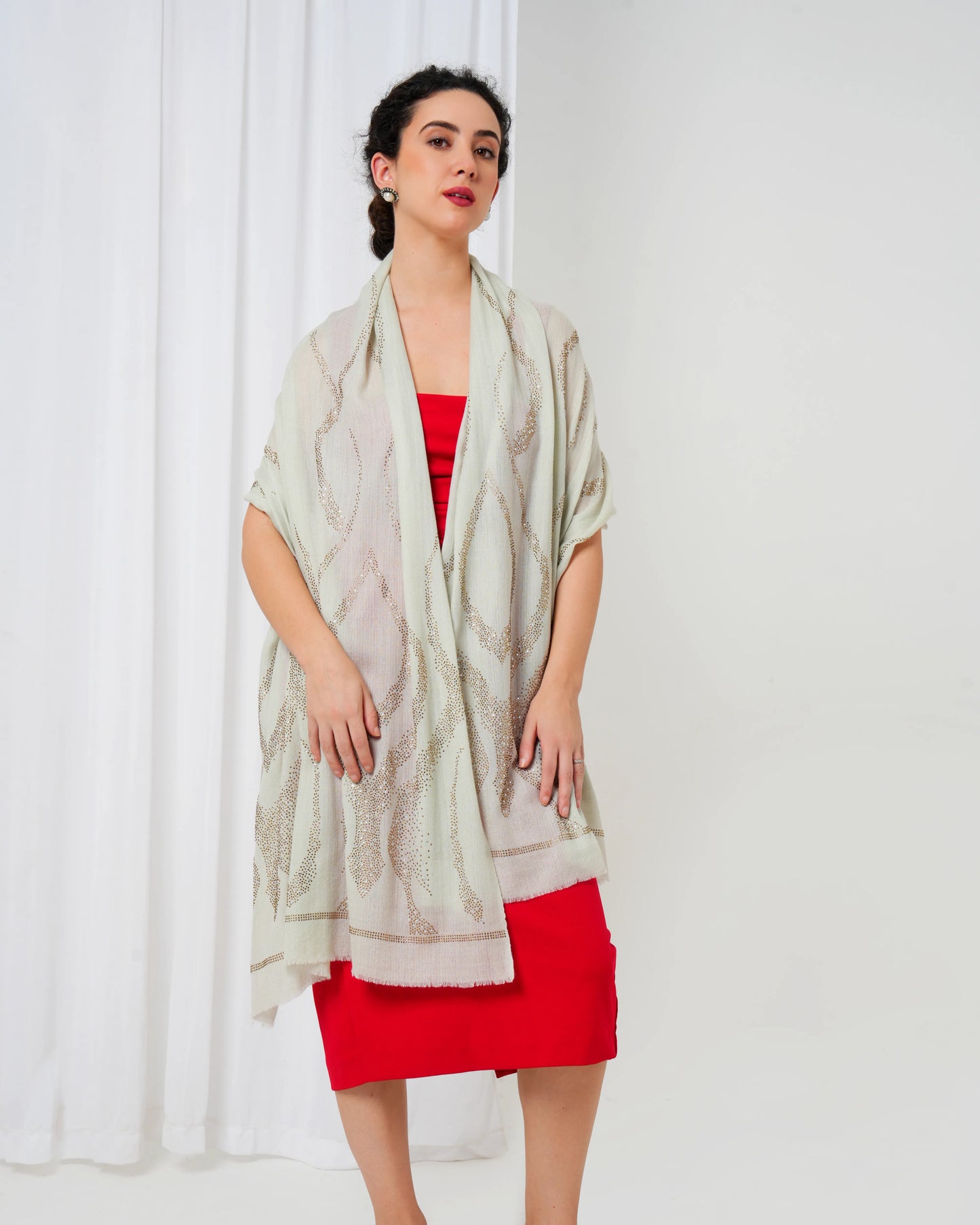 Woman wearing a light-colored scarf over a red dress against a white curtain background