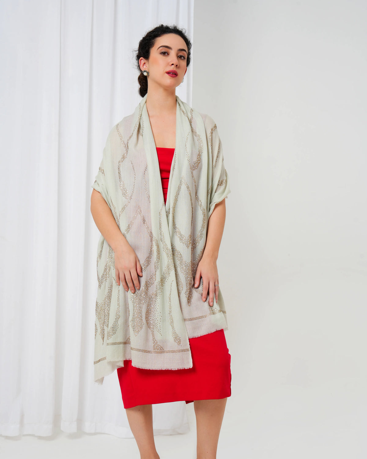 Woman wearing a light-colored scarf over a red dress against a white curtain background