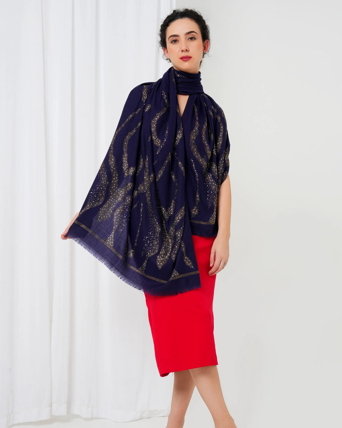 Woman wearing a navy blue scarf with gold patterns over a red dress on a white background