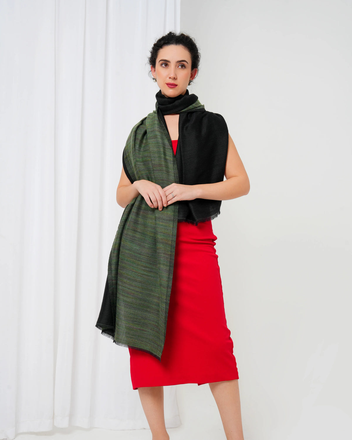 Woman wearing a green scarf, black top, and red skirt against a white background