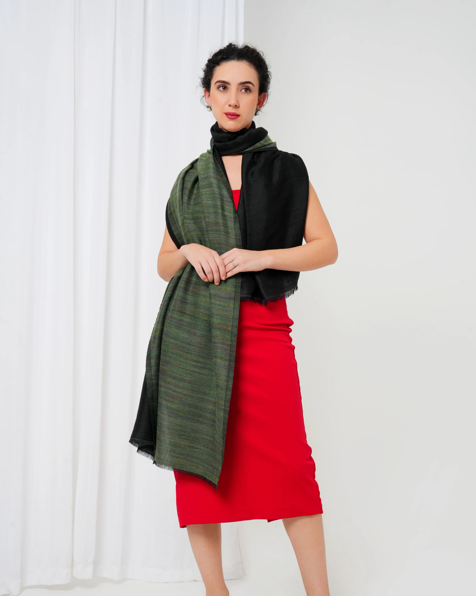 Woman wearing a green scarf, black top, and red skirt against a white background
