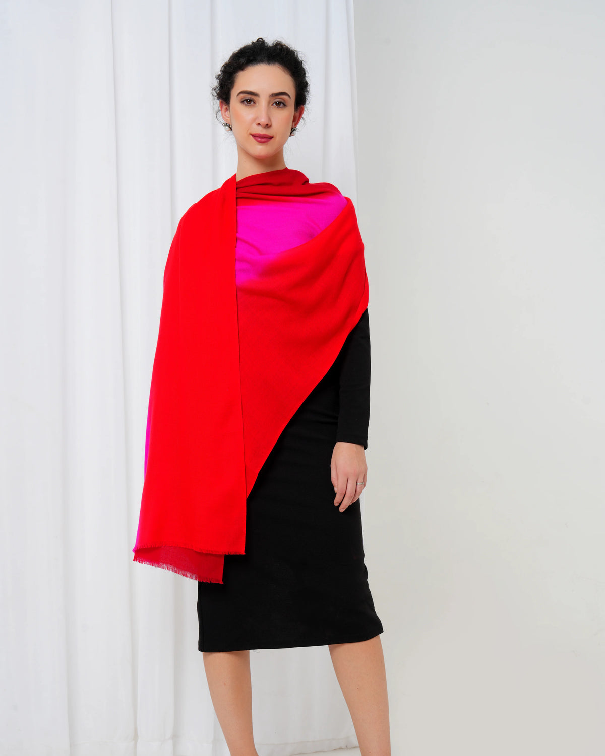 Woman wearing a red and pink shawl over a black dress against a white curtain background