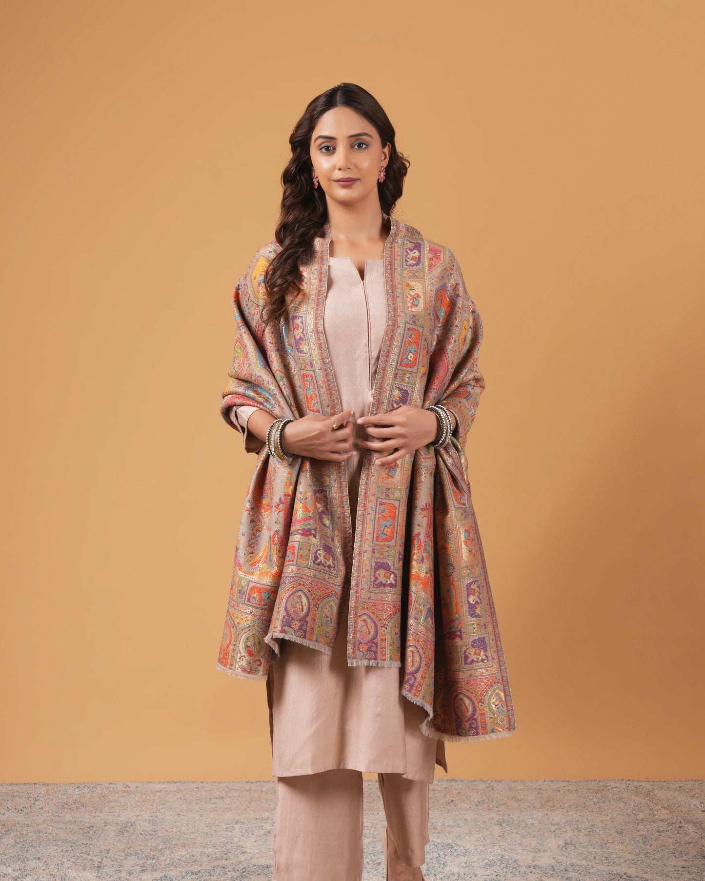 Woman wearing a patterned shawl over a plain outfit against a beige background