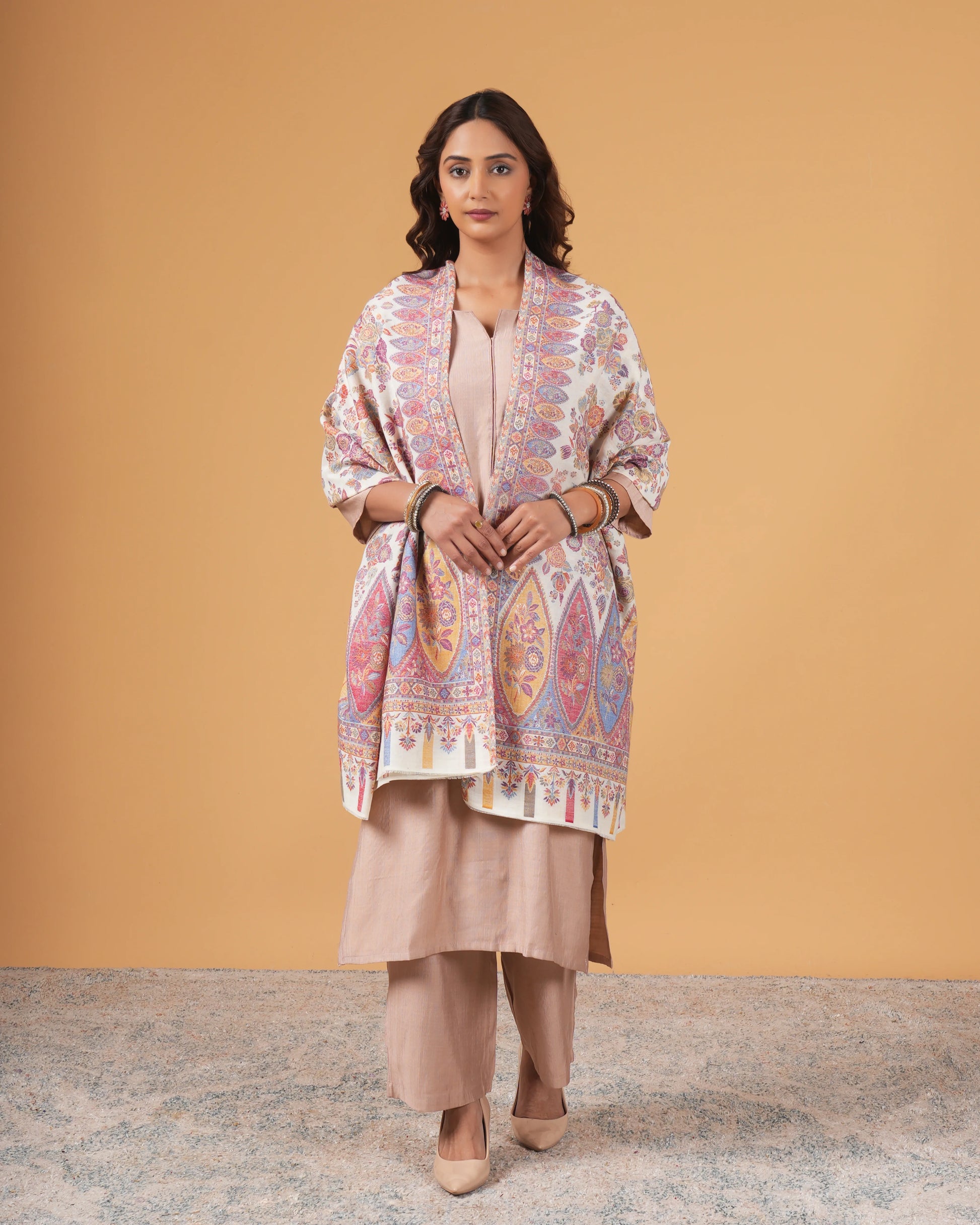 Woman wearing a patterned shawl over a beige outfit against a mustard yellow background