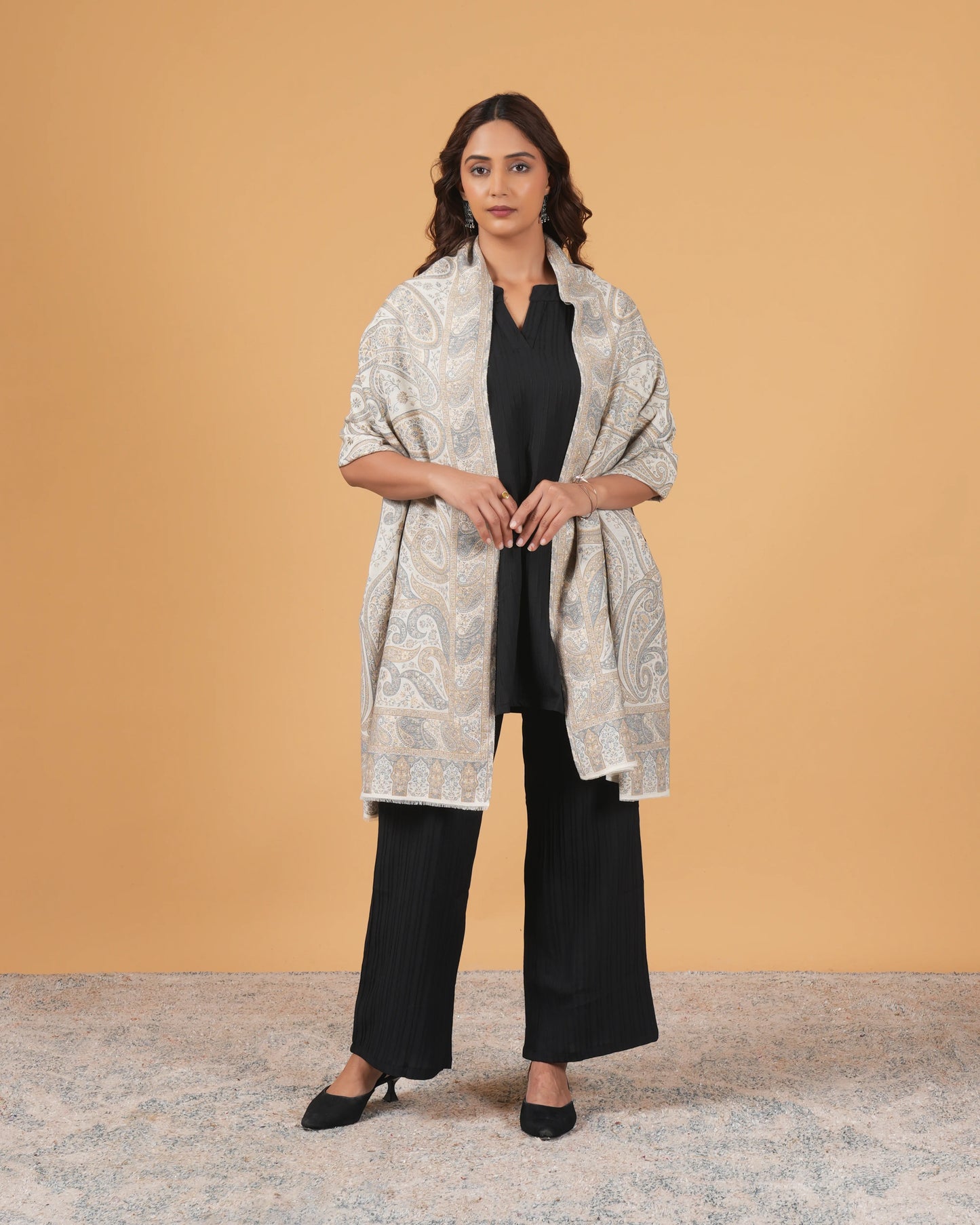 Woman wearing a patterned shawl over a black outfit against a beige background