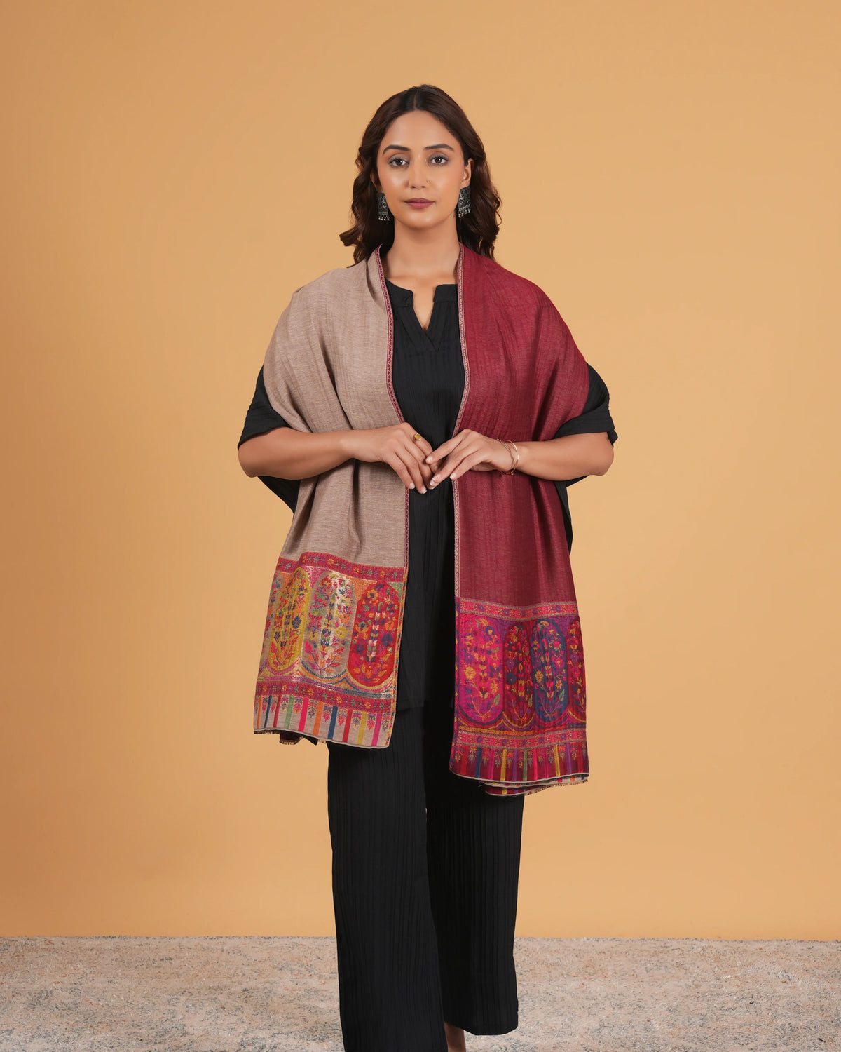 Woman wearing a patterned shawl over a black outfit on a beige background