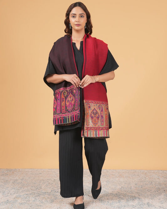 Woman wearing a red and black traditional outfit with a patterned shawl against a beige background