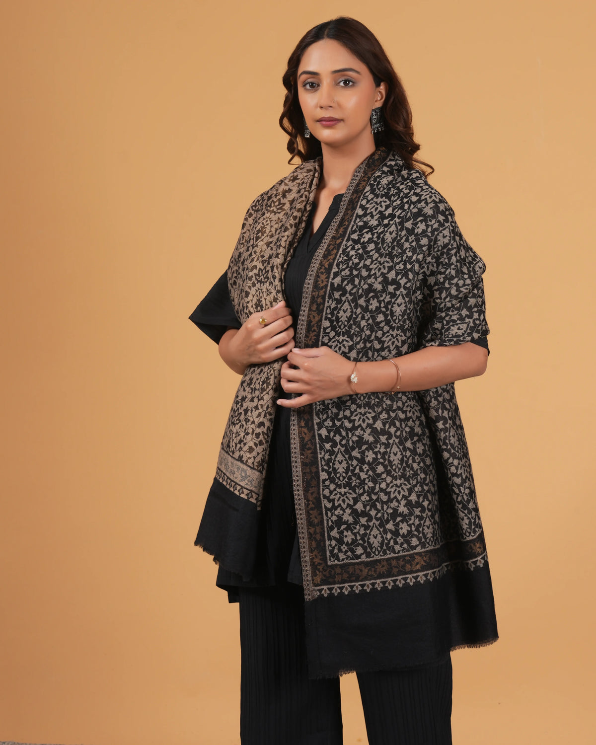 Woman wearing a black and white patterned shawl over a black outfit on a beige background