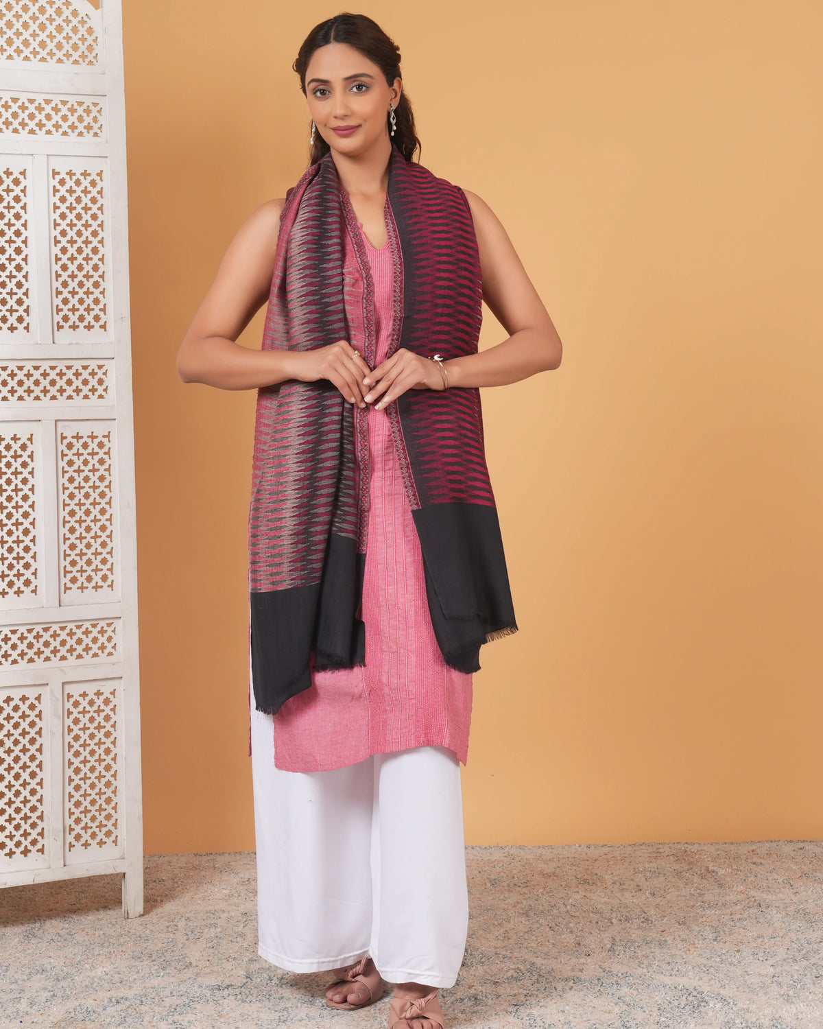 Woman wearing a pink kurta with a black and red scarf against an orange wall.