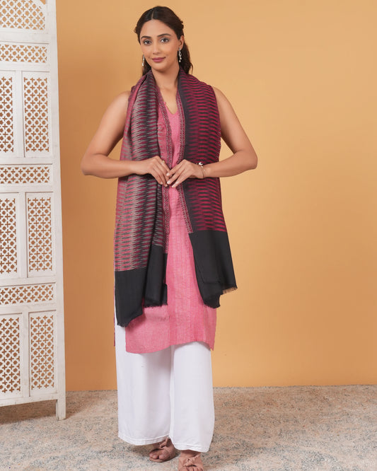 Woman wearing a pink kurta with a black and red scarf against an orange wall.