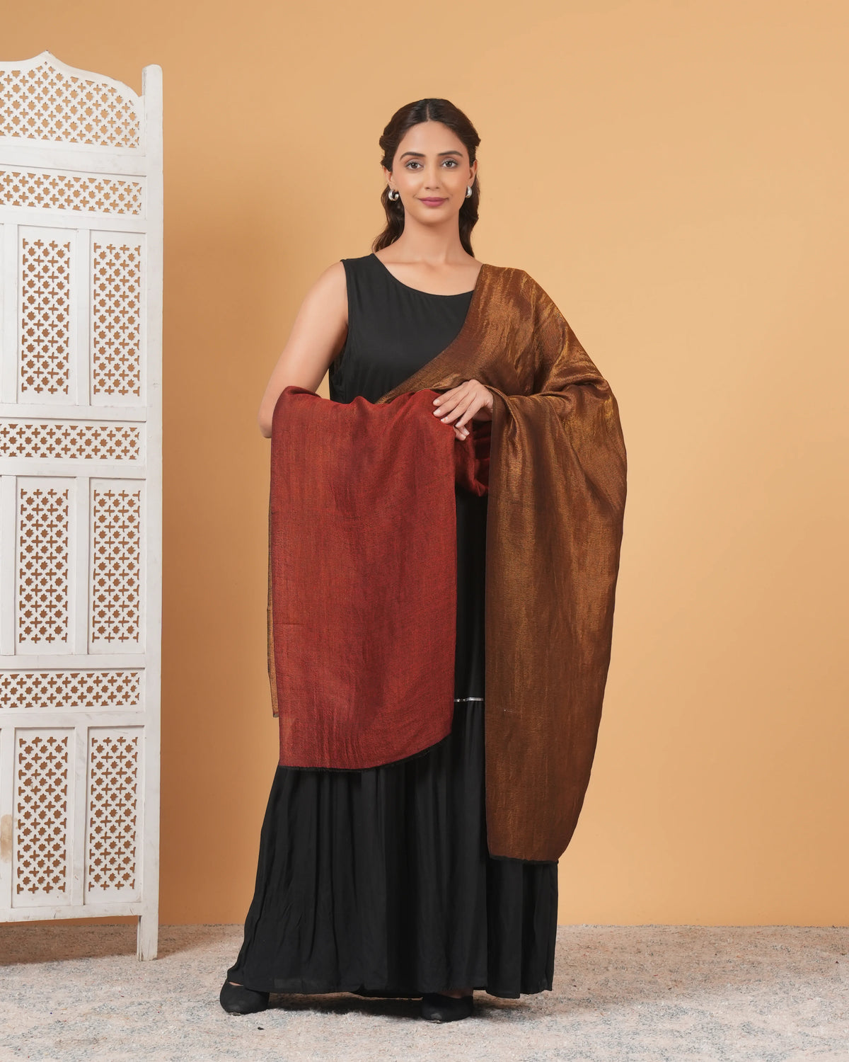 Woman holding a brown scarf over a black outfit against an orange wall.